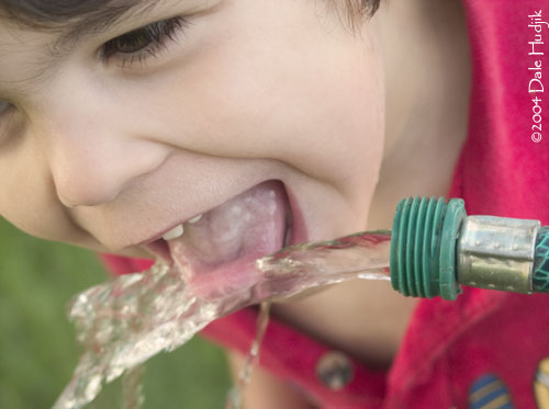 boy drinking from garden hose